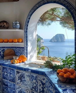 Blue tiled Mediterranean kitchen with arched window view of sea and rocky island, oranges on counter