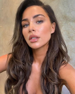 Close-up selfie of a young woman with long brown wavy hair and blue eyes