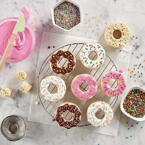 Colorful frosted donuts with sprinkles on cooling rack, overhead view on marble counter