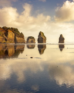 Sea stacks and cliffs reflected on wet beach sand beneath cloudy sky
