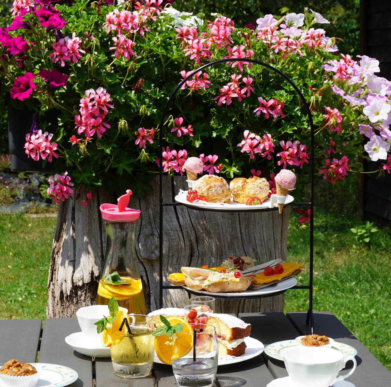 Three-tier tea stand with desserts and savories in garden with flowering plants
