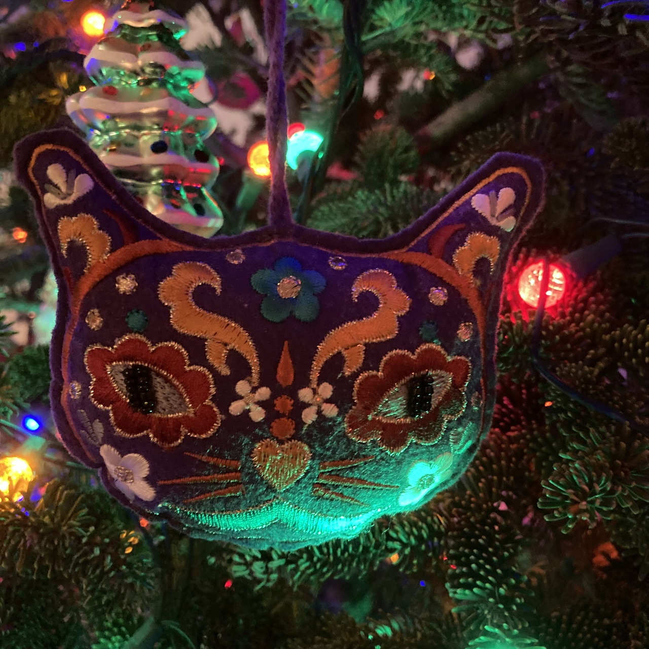 Cat-shaped ornament hanging on a Christmas tree with colorful lights