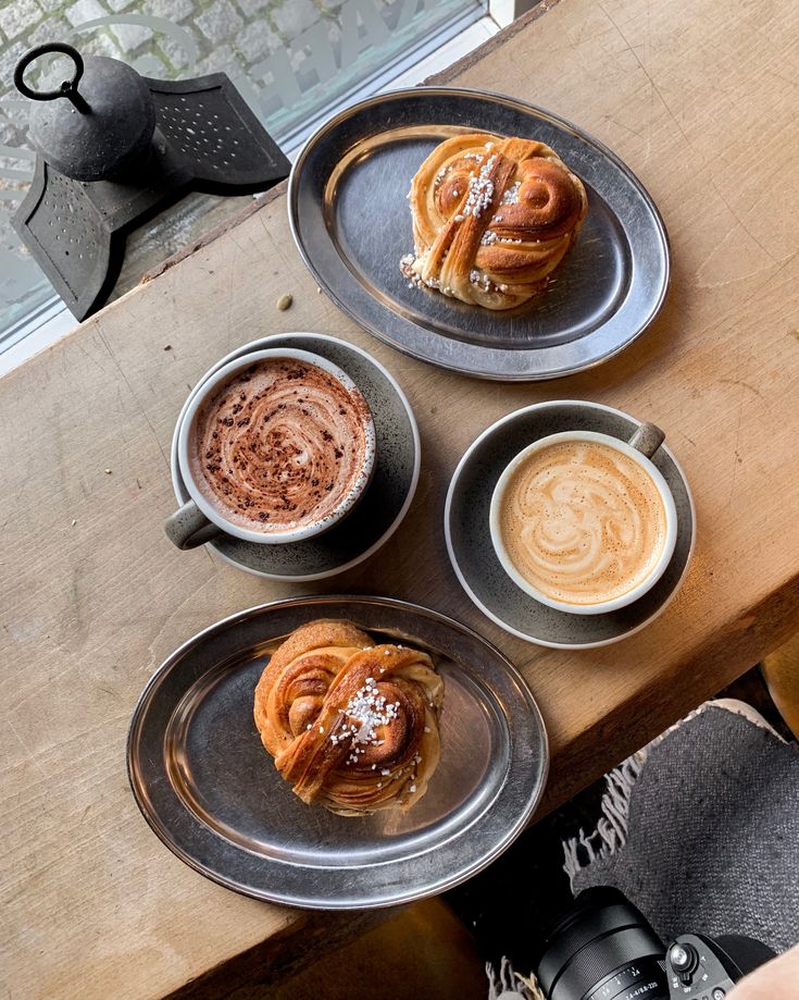 Top-down view of two cinnamon buns and two coffee drinks on a wooden café table