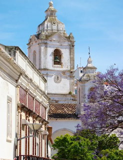 White Portuguese baroque church with twin bell towers and dome, purple jacaranda tree in foreground