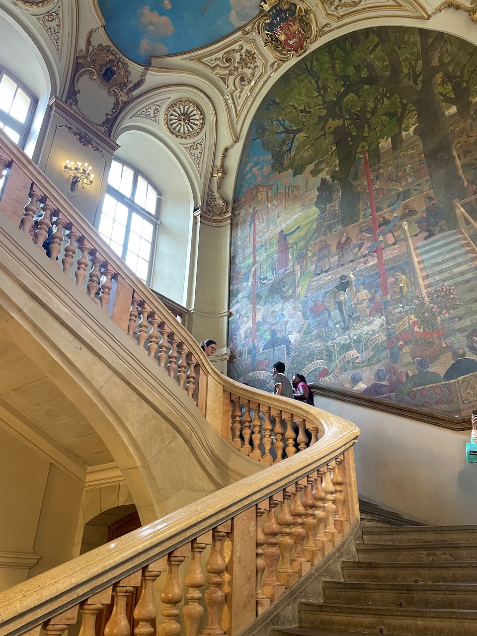 Grand marble staircase with balustrade in a museum with a large mural painting on the wall