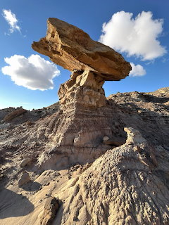 Hoodoo balanced rock formation in desert landscape with blue sky and clouds