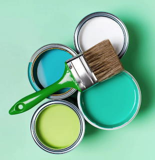 Four open paint cans in various colors with a paintbrush on green surface