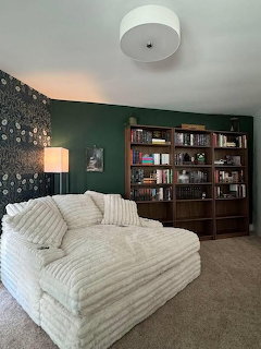 Cozy room with white corduroy sofa, wooden bookshelves, green wall, and floral wallpaper