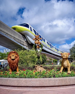 Disney monorail above Lion King topiary sculptures with cloudy sky background