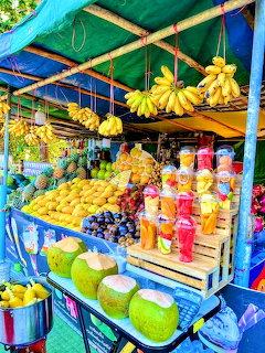 Colorful Thai fruit cart with hanging banas, mangoes, coconuts, and fresh juice cups on display