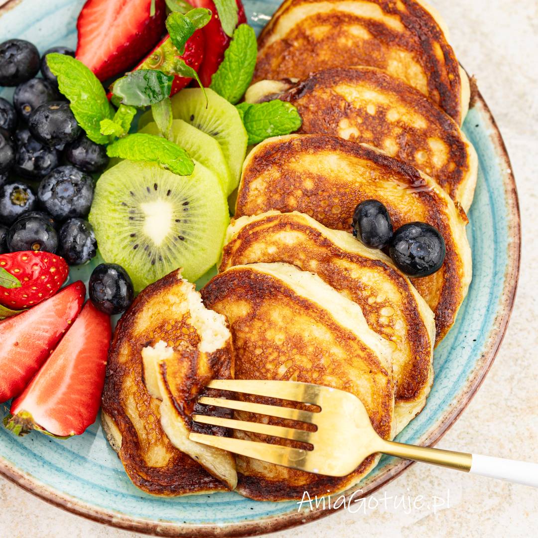 Golden pancakes arranged on blue plate with strawberries, blueberries, kiwi and mint, fork taking a bite