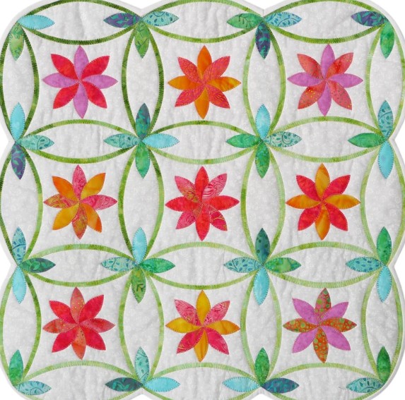 Decorative quilt with nine floral star blocks in warm colors connected by green vine pattern on white fabric