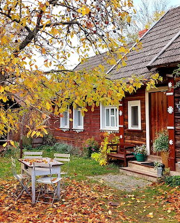 Red wooden cottage with white windows in autumn garden with golden leaves and rustic bench