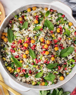 White bowl of rice pilaf garnished with pomegranate seeds, chickpeas, and fresh mint leaves