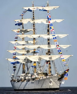 White tall ship with multiple masts, white sails, and colorful signal flags at sea