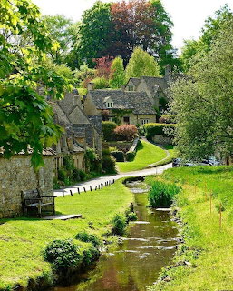 Traditional stone cottage beside a stream in a garden with green lawns and trees