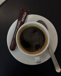 Top view of black coffee in a white cup on a saucer with a spoon and sugar stick