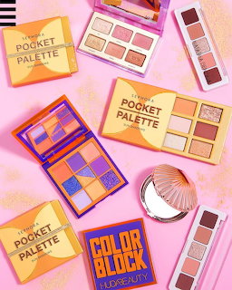 Several eyeshadow palettes and makeup brushes arranged flat lay style on a pink background