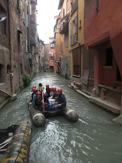 Boat carrying passengers through a narrow canal between old colorful buildings in Bologna with a swan nearby