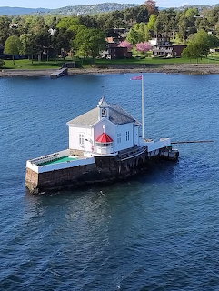 White lighthouse on floating platform in Norwegian fjord with forested shore