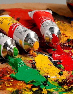 Three paint tubes squeeze colorful oil paints onto a wooden artist palette with mixed colors