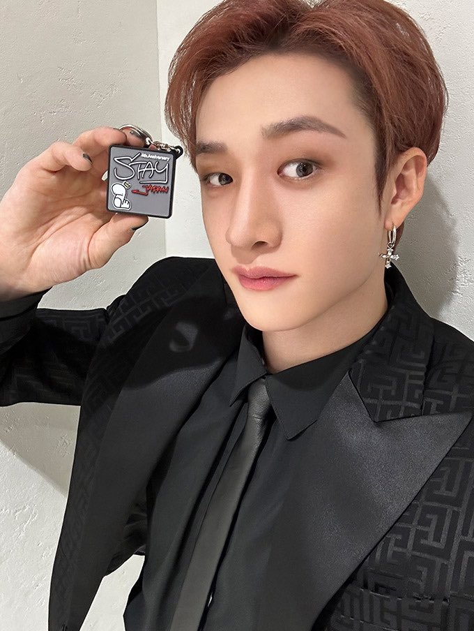 Portrait of Bang Chan from Stray Kids in black formal wear holding a metallic object against a light background