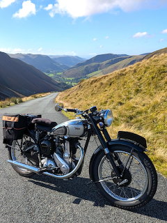 Vintage BSA B33 motorcycle on a mountain road with hills under a blue sky