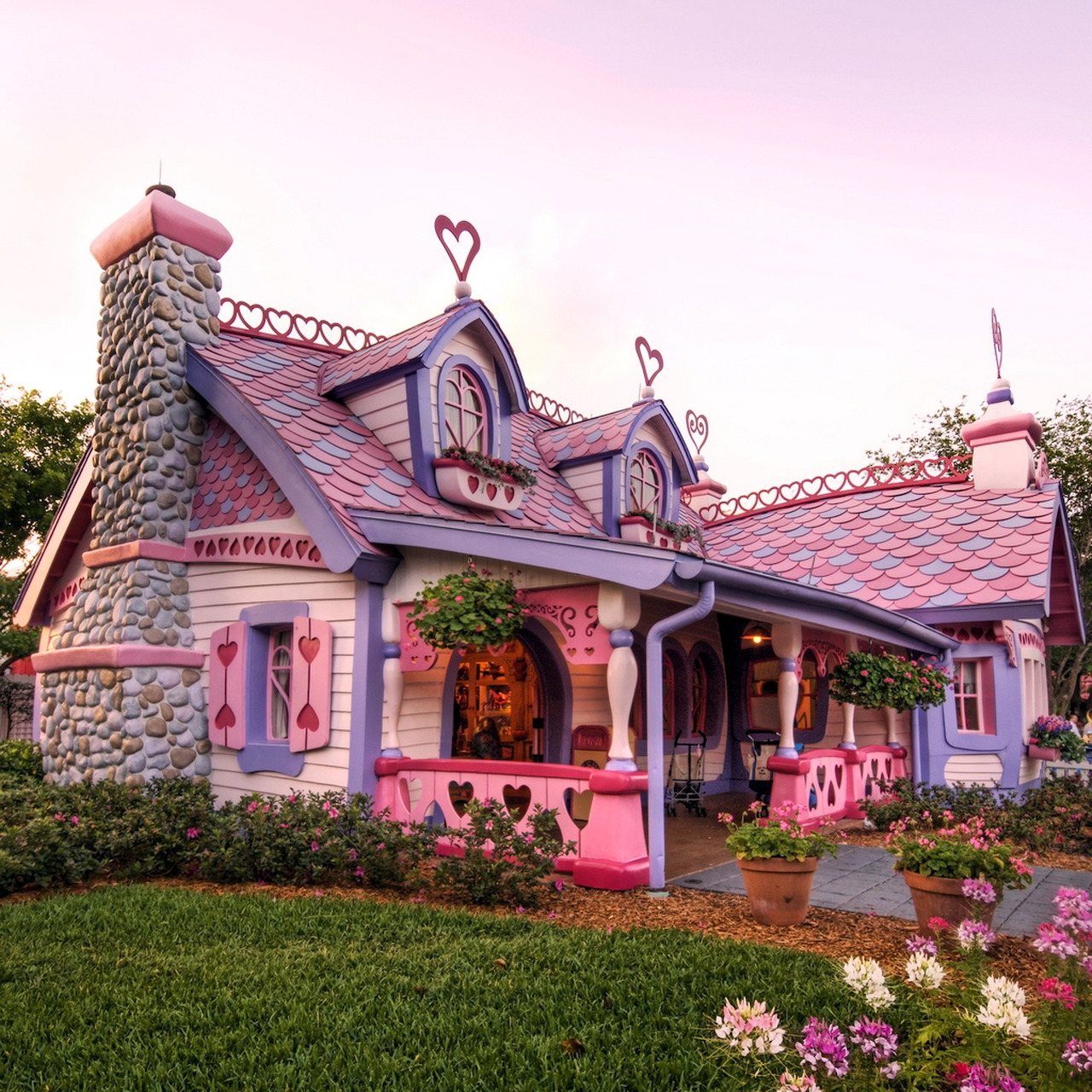 Pink cottage with ornate roof, stone chimney, and colorful flower garden in front yard