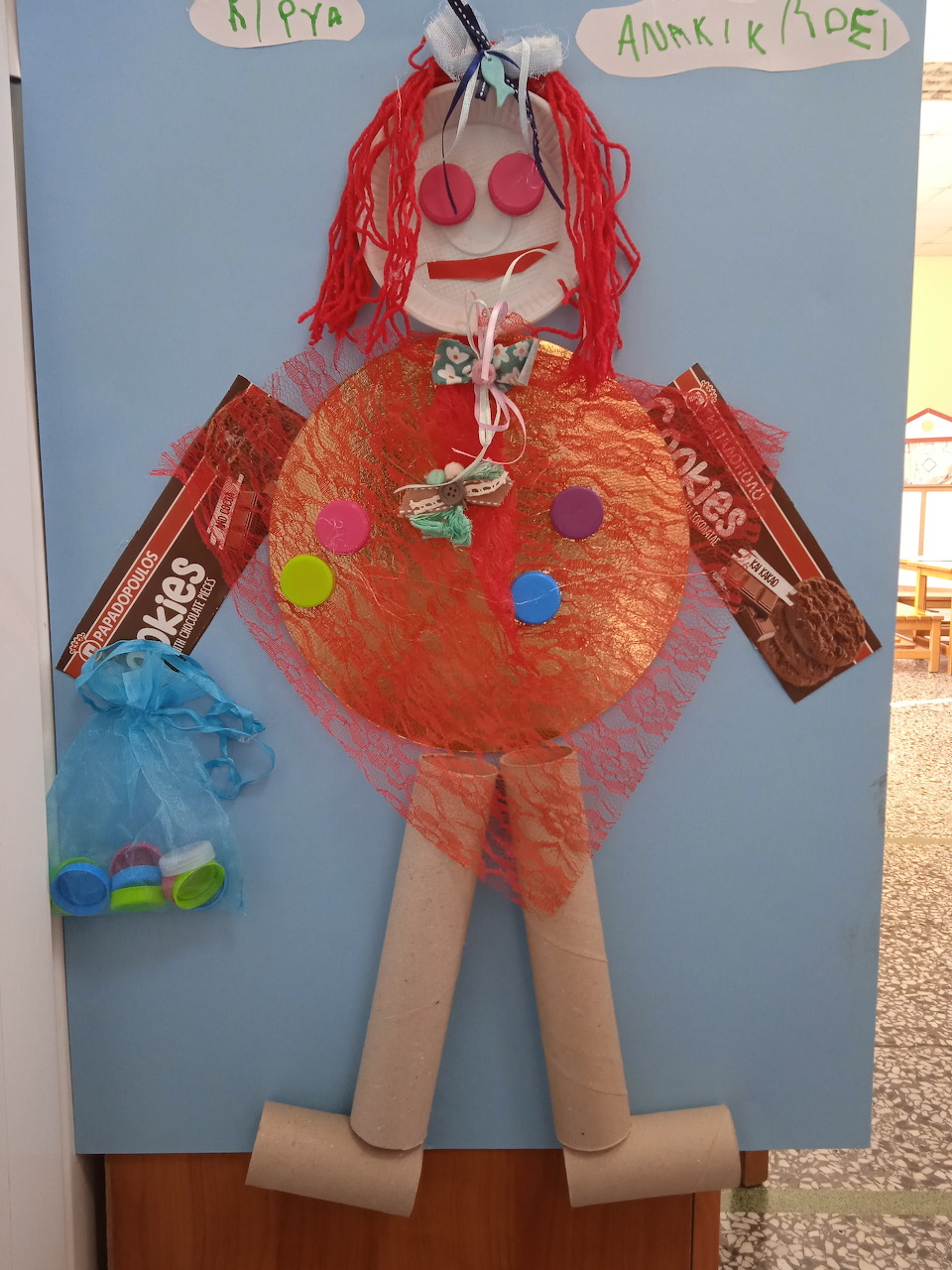 Handmade puppet figure made from recycled materials including cardboard tubes, orange netting, and colorful dots