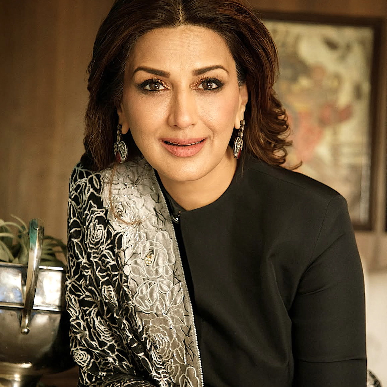 Smiling woman in a black outfit with a patterned shawl and earrings, posed indoors