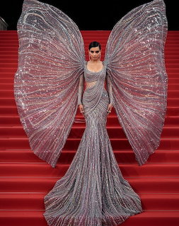 Woman in silver gown with large translucent butterfly wings standing on red staircase