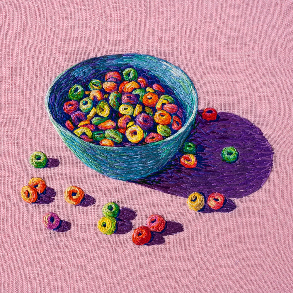 Embroidered bowl filled with multicolored cereal loops on pink fabric