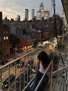 Woman on balcony viewing New York City skyline at twilight with lit buildings