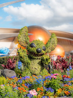 Green topiary shaped like Stitch character surrounded by vibrant flowers at Epcot theme park