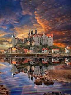 Castle complex reflected in river water under dramatic sunset sky with orange and blue clouds
