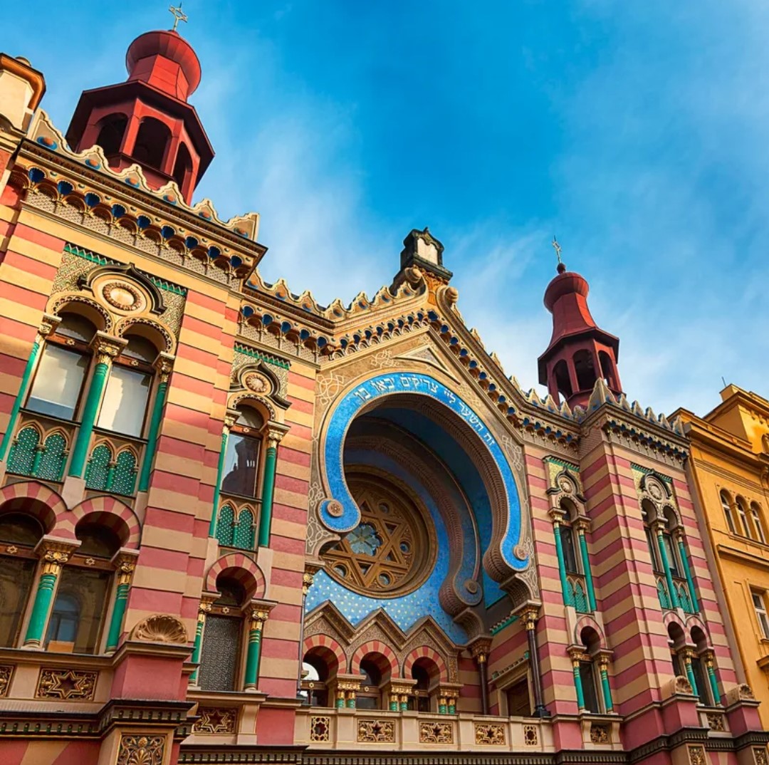 Colorful historic synagogue with ornate Moorish architecture, striped pink walls, and decorative towers under blue sky