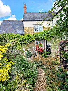 Gravel path through a lush cottage garden leading to a stone house with climbing plants