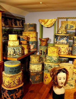 Stacks of colorful antique hatboxes with floral and scenic patterns beside a wooden milliner head