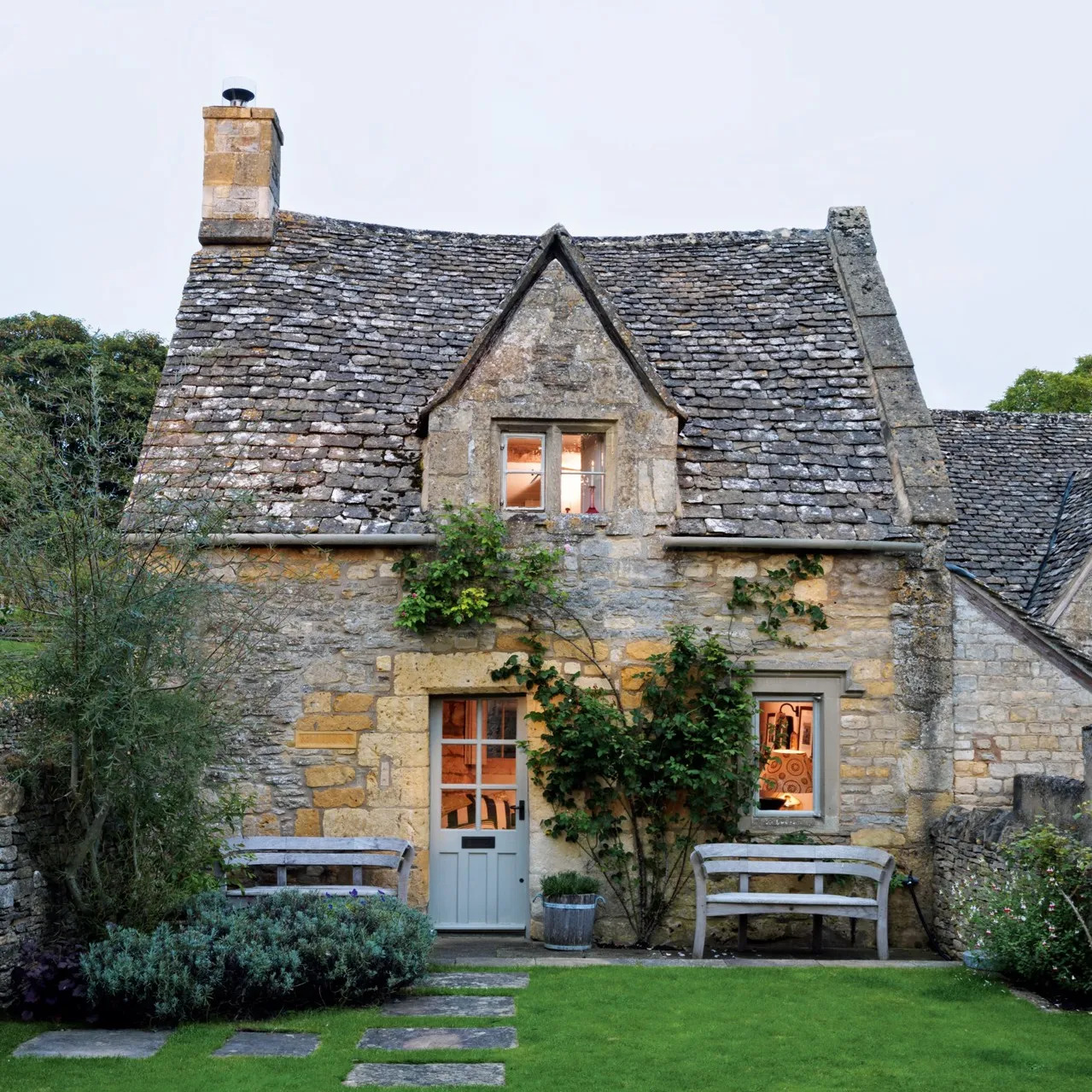 Historic Cotswold stone cottage with blue door and garden benches