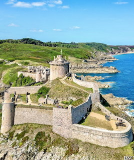 Aerial view of Fort La Latte medieval castle on a rocky coastal cliff with blue ocean and green hills