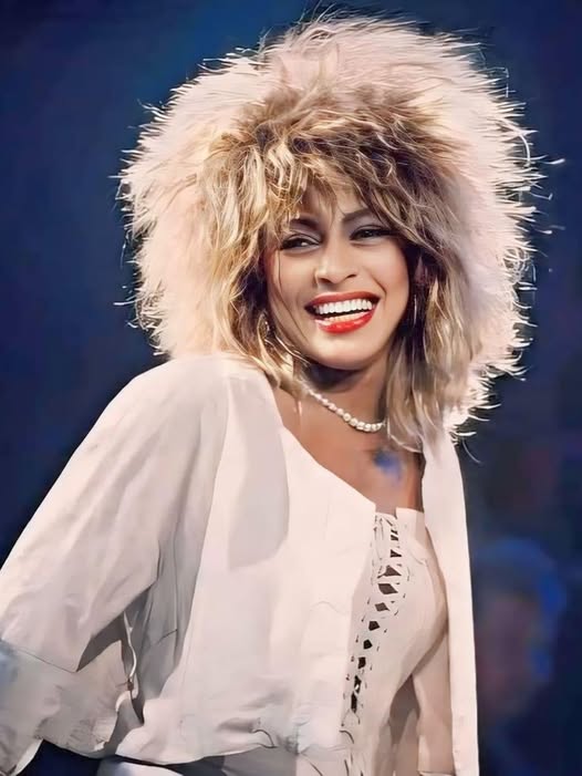 Smiling woman with large blonde fluffy hat and white blouse, stage performer portrait