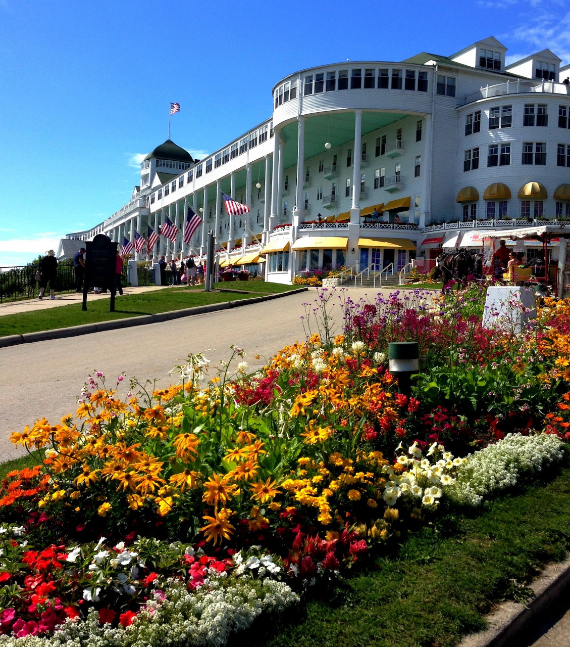 White colonial hotel with columned porch, yellow awnings, and colorful flower gardens in foreground under blue sky