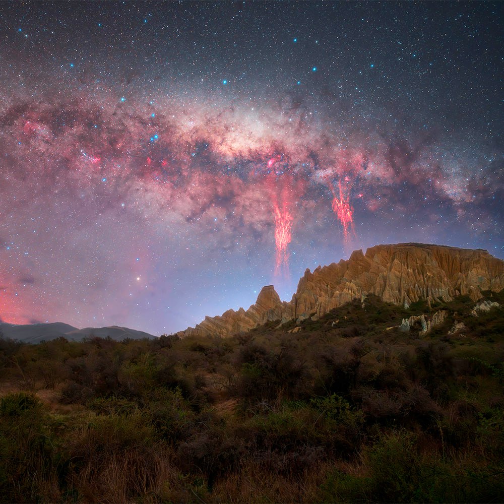 Milky Way galaxy in pink and blue hues arching over desert mesa at night