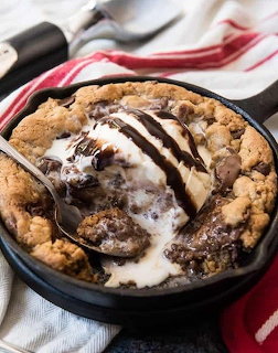 Chocolate chip skillet cookie with melting vanilla ice cream and chocolate drizzle in cast iron pan
