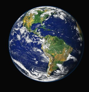 Satellite photograph of Earth showing North and South America with clouds, oceans, and continents visible
