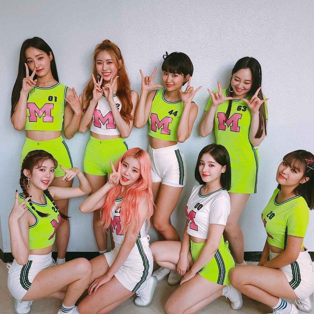 Eight Momoland members posing in neon green and white sporty outfits in a studio