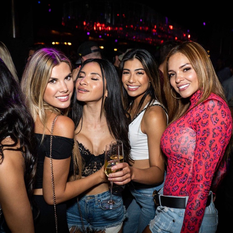 Five women smiling together at a nightclub event with dark background lighting