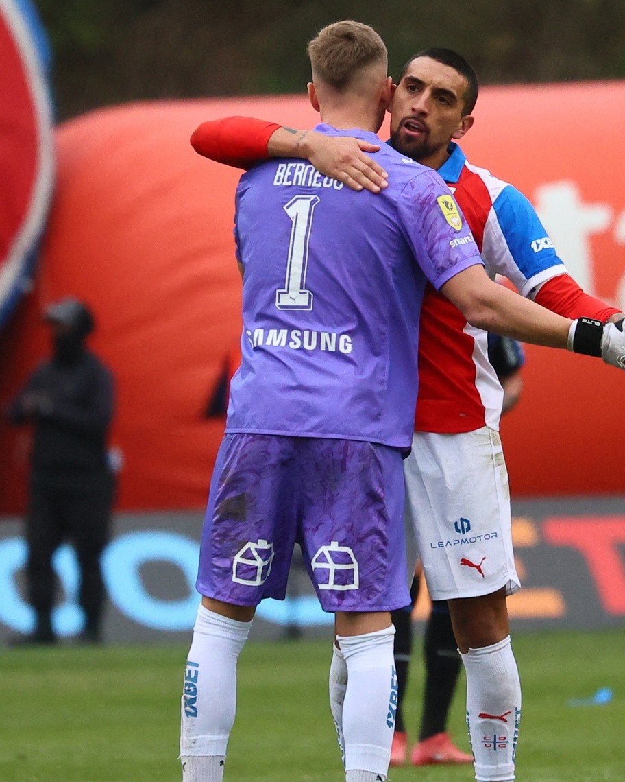 Two soccer players hugging on the field, with goalkeeper Bernedo in a purple jersey seen from behind