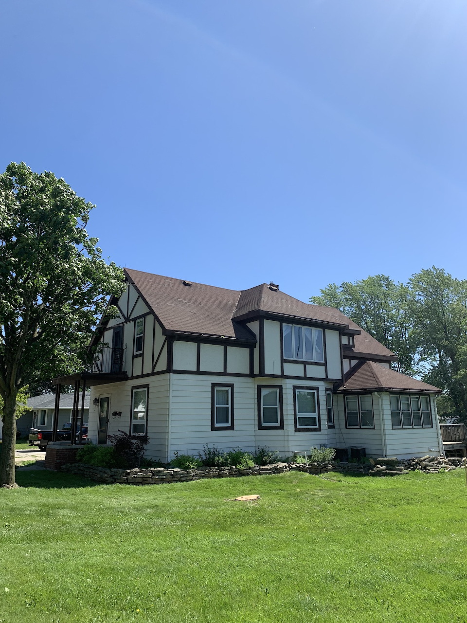 White Tudor-style farmhouse with dark brown trim and steep roof on a green lawn under blue sky