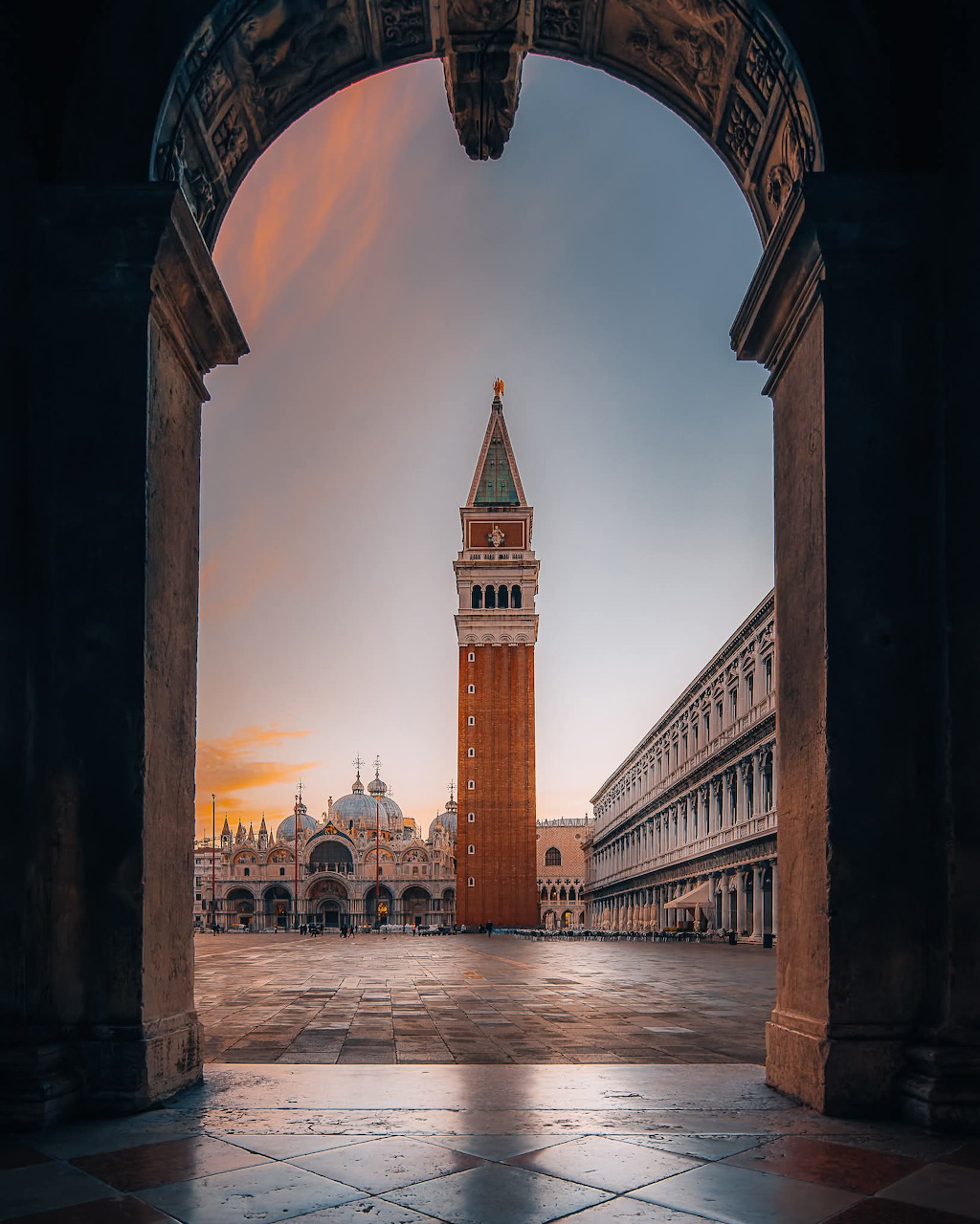 St Mark's Campanile and Basilica in Venice seen through a stone arch at sunset